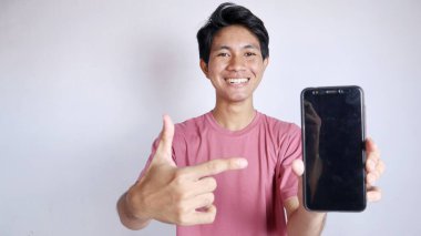 Beyaz arka plandaki akıllı telefonu işaret eden hareketli heyecanlı Asyalı adam.