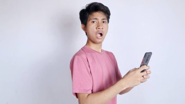 Asyalı bir adam beyaz arka planda jest yaparak ve akıllı telefon tutarak şoka girdi.