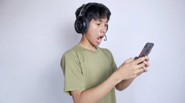 Asyalı adamın kulaklık kullanması ve beyaz arka planda akıllı telefon oynaması şok edici.