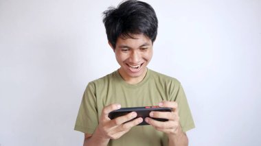 Heyecanlı Asyalı adam beyaz arka planda cep telefonu oyunu oynuyor