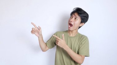 Genç Asyalı adam şok oldu. İzole edilmiş beyaz bir arka planla sağ tarafı işaret ediyor.