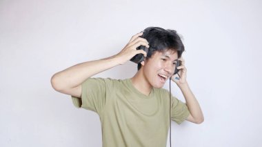 Asyalı adam, beyaz arka planda kulaklık takıp müzik dinleyerek heyecan verici bir şekilde mutlu.