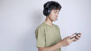 ciddi Asyalı adam kulaklık kullanıyor ve beyaz arka planda cep telefonu oyunları oynuyor.