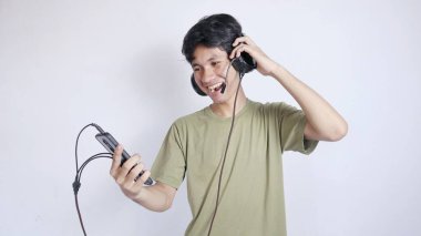 Heyecanlı Asyalı adam kulaklık takıyor ve beyaz arka planda akıllı telefon tutuyor.