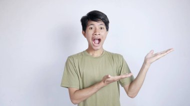 Şok olmuş genç Asyalı adam, beyaz bir arka planla sol tarafı işaret ediyor.