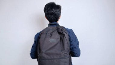 İzole edilmiş beyaz bir arka planda çanta taşıyan Asyalı genç bir erkek öğrenci.