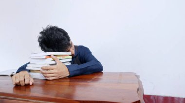 Genç yakışıklı Asyalı erkek yorgun, yorgun, masada uyuyakalmış ve kitaplarda izole edilmiş beyaz arka plan.