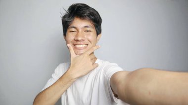 Genç Asyalı adam kamerasıyla izole edilmiş beyaz bir arkaplanda selfie çekiyor.