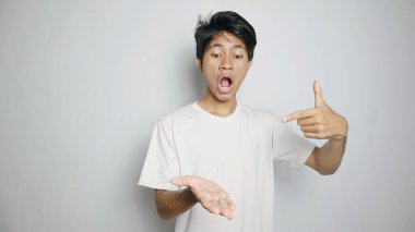 Beyaz gömlekli genç, şok olmuş Asyalı bir adam avucunun içini göstererek izole edilmiş beyaz bir arka planı var.