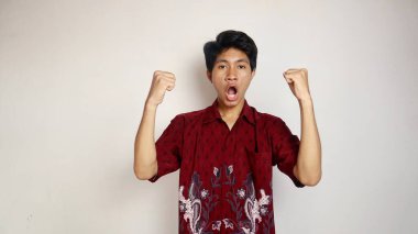 Batik gibi giyinmiş yakışıklı Asyalı genç adam. İki eli havada poz veriyor. Çok heyecanlı ve mutlu.
