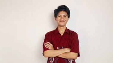 Batik gibi giyinmiş yakışıklı genç Asyalı izole beyaz arka planda çapraz kollara poz veriyor.