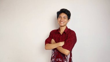 Batik gibi giyinmiş yakışıklı genç Asyalı izole beyaz arka planda çapraz kollara poz veriyor.