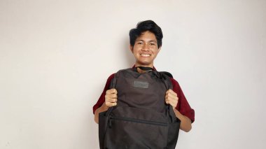 Batik giysili yakışıklı genç adam, beyaz arka planda, öndeki çantayı tutuyor.