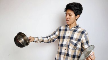 Asyalı genç bir adam beyaz bir arka planda tava tutarken şok oldu.