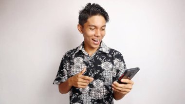 Batik tişört giyen yakışıklı genç ve yakışıklı adam izole edilmiş beyaz arka planda akıllı telefon pozu veriyor ve tutuyor.