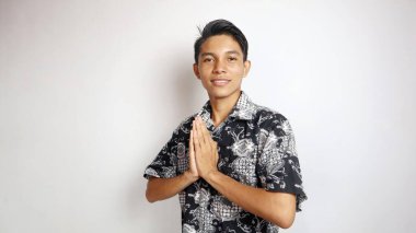 Batik gibi giyinmiş yakışıklı Asyalı genç adam, izole edilmiş beyaz arka planda bir jest yapıyor.