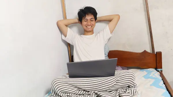 Relaxed young Asian men are playing, using, watching, video calling, discussing using a laptop on the bed mattress