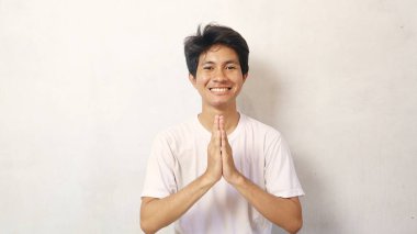 Beyaz tişörtlü gülümseyen Asyalı genç adam izole beyaz arka planda poz veriyor.