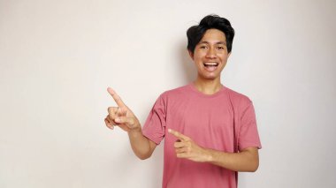 Genç yakışıklı Asyalı adam mutlu, neşeli ve coşkulu pozlar izole edilmiş beyaz bir arkaplanı işaret ediyor. Kırmızı bir gömlek giyiyor.