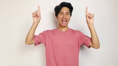 Heyecanlı genç yakışıklı Asyalı mutlu, neşeli ve heyecanlı pozlar izole beyaz arka planı ile üst tarafı işaret ediyor. Kırmızı bir gömlek giyiyor.