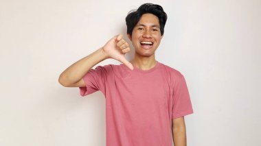 Heyecanlı genç yakışıklı Asyalı adam mutlu, neşeli ve heyecanlı poz vererek izole edilmiş beyaz arka planla baş parmaklarını aşağı gösteriyor. Kırmızı giysiler giyiyor.