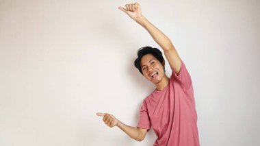 Genç yakışıklı Asyalı adam mutlu, neşeli ve coşkulu pozlar izole edilmiş beyaz bir arkaplanı işaret ediyor. Kırmızı bir gömlek giyiyor.