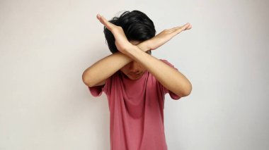 İzole edilmiş beyaz bir arka planda çapraz kollarla poz veren genç bir Asyalı. Reddetmek, hayır demek, jesti engellemek. Kırmızı bir gömlek giyiyor.