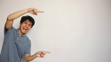 Yakışıklı Asyalı genç adam beyaz bir arka planda yan tarafı işaret ediyor.