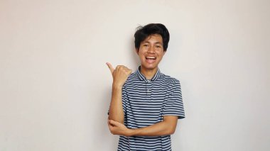 Yakışıklı Asyalı genç adam izole edilmiş beyaz bir arka planda mutlu bir şekilde kenarı işaret ediyor.