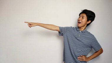 Yakışıklı Asyalı genç adam izole edilmiş beyaz bir arka planda mutlu bir şekilde kenarı işaret ediyor.