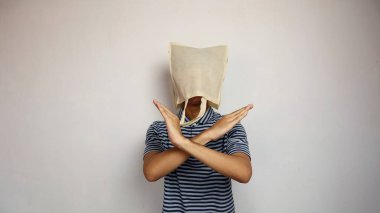 Kafasında alışveriş torbası olan genç Asyalı bir adam kollarını çapraz yapıp izole edilmiş beyaz bir arka plana sahip.