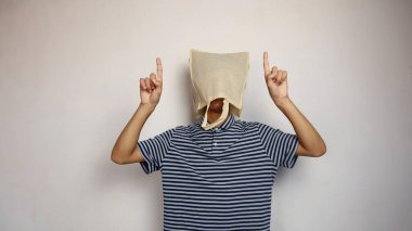 Kafasında alışveriş torbası olan genç Asyalı bir adam, el hareketi ile izole edilmiş beyaz bir arkaplanı işaret ediyor.