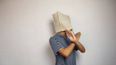 Kafasında alışveriş torbası olan genç Asyalı bir adam kollarını çapraz yapıp izole edilmiş beyaz bir arka plana sahip.