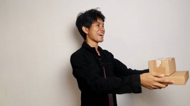 Heyecanlı Asyalı genç adam, kargo kutusu paketini izole edilmiş beyaz arka planda tutuyor ve veriyor. Teslimat kuryesi ve nakliye hizmeti konsepti