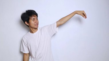 Genç Asyalı bir adam eli boş bir yerde bir şey tutuyor ve izole edilmiş beyaz arka planda ona bakıyor, boşluğu kopyalıyor.