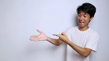 Beyaz gömlekli heyecanlı genç Asyalı adam. Komik bir yüz ifadesi var. Avuç içi izole beyaz arka plana işaret ediyor.