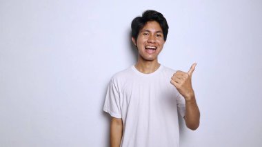 excited young asian man in white shirt with funny expression showing thumbs up okay, great, cool, steady, winning isolated white background clipart