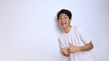excited young asian man in white shirt with funny expression showing thumbs up okay, great, cool, steady, winning isolated white background clipart