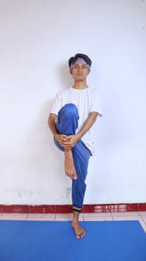 Beyaz gömlekli genç adam evdeki spor minderinde bacaklarını ısıtıyor.