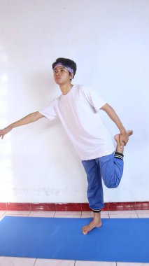 Beyaz gömlekli genç adam evdeki spor minderinde bacaklarını ısıtıyor.