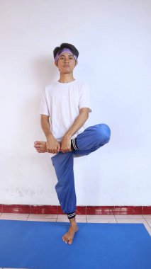 Beyaz gömlekli genç adam evdeki spor minderinde bacaklarını ısıtıyor.