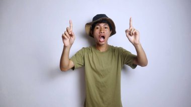 Asyalı heyecanlı genç bir adam, izole edilmiş beyaz bir arkaplanı işaret eden bir şapka takıyor.
