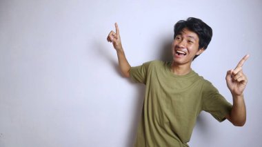 Heyecanlı Asyalı genç adam hareketleriyle izole edilmiş beyaz sırtı işaret ediyor.