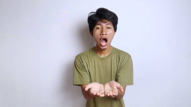 İzole edilmiş beyaz bir arkaplanda açık el hareketleriyle ileri bakan Asyalı genç bir adamın komik ifadesi.