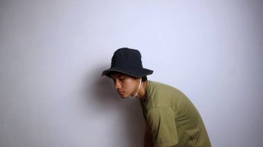 Yan bakış: Şapkalı genç Asyalı adam uyuşuk, yorgun, kamburlaşmış, izole beyaz arka planı var.