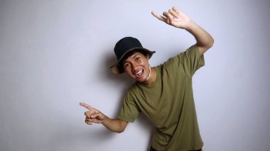 Asyalı heyecanlı genç bir adam, izole edilmiş beyaz bir arkaplanı işaret eden bir şapka takıyor.