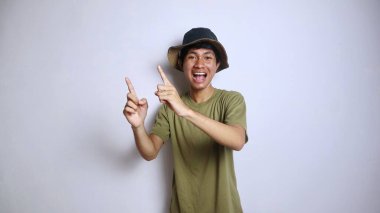 Asyalı heyecanlı genç bir adam, izole edilmiş beyaz bir arkaplanı işaret eden bir şapka takıyor.