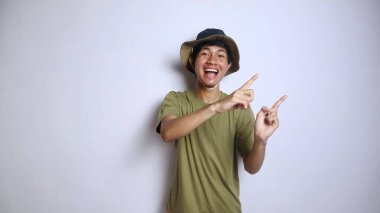 Asyalı heyecanlı genç bir adam, izole edilmiş beyaz bir arkaplanı işaret eden bir şapka takıyor.