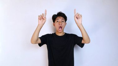 Siyah tişörtlü genç Asyalı şok olmuş. El hareketleriyle izole edilmiş beyaz arka planı işaret ediyor. Boşluğu kopyala