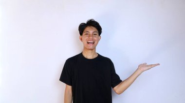 Heyecanlı Asyalı genç adam, siyah gömlekli açık el hareketleriyle bir ürün, fotokopi alanı, reklamcılık, izole edilmiş beyaz arka planlı pazarlama gösteriyor.